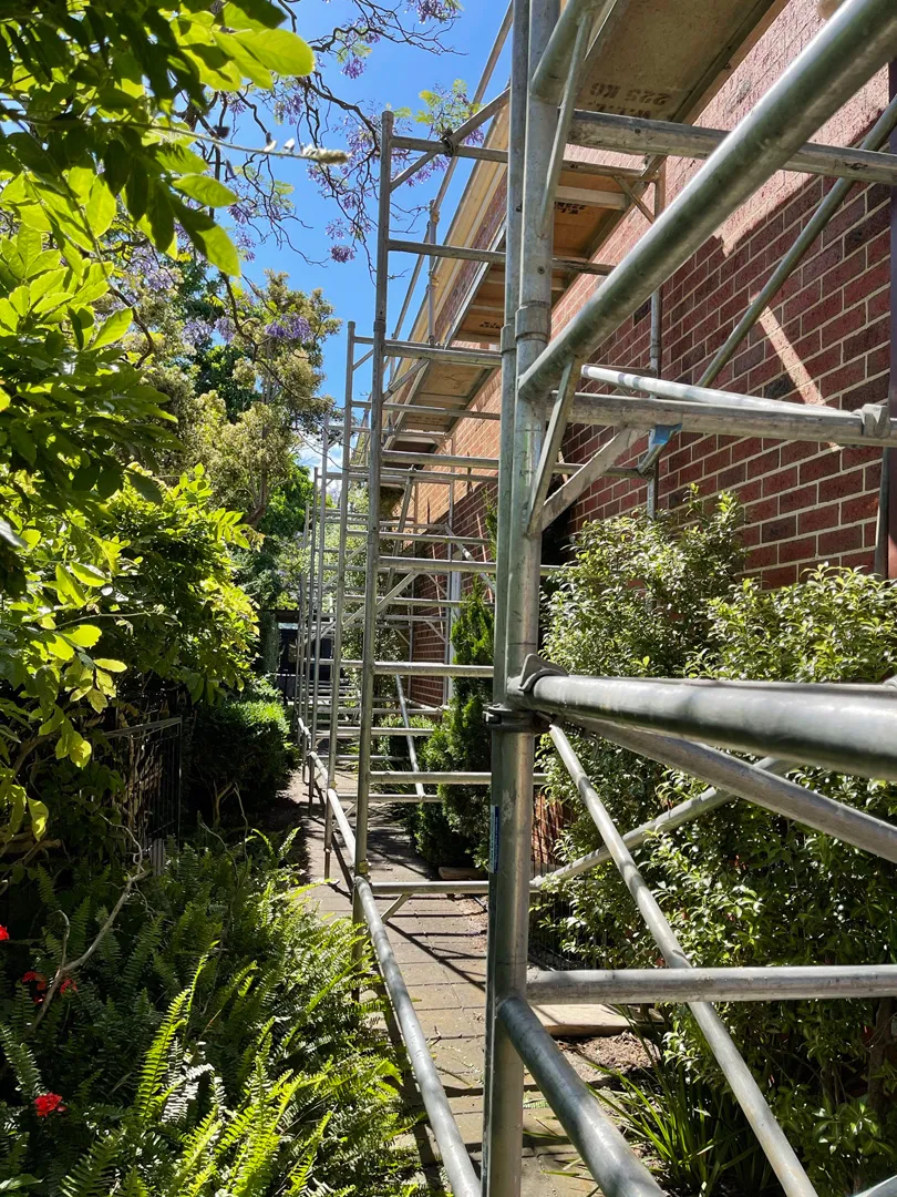 Narrow side passage, full-height scaff against heritage brick. — Sorrento